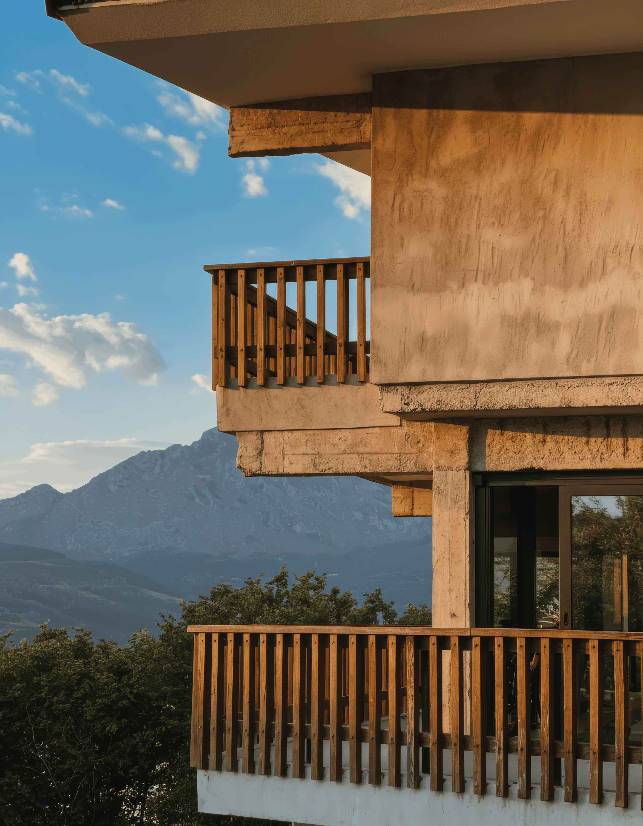 Dos balcones con barandillas de madera, vigas vistas y montañas al fondo.
