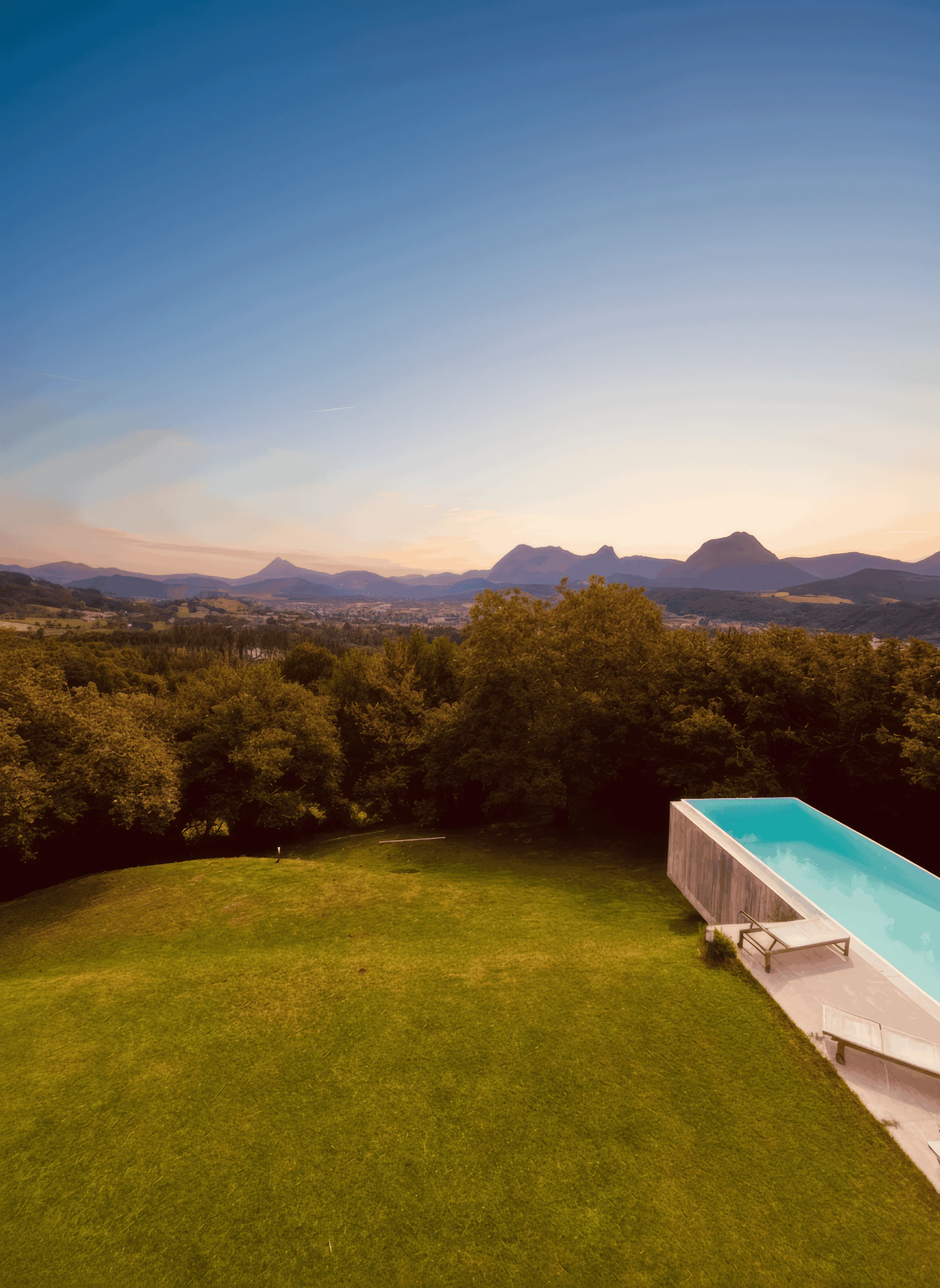 Jardín de césped con la piscina en un lateral y las montañas al fondo.