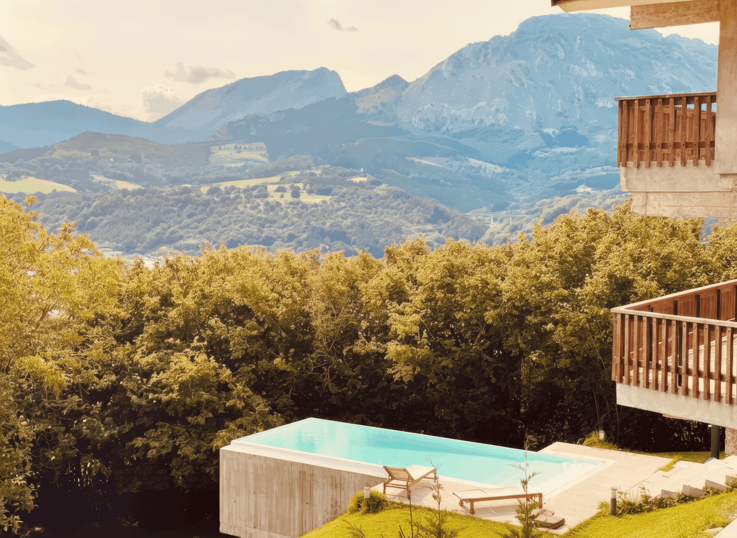 Piscina de hormigón junto a la casa, con tumbonas y montañas al fondo.