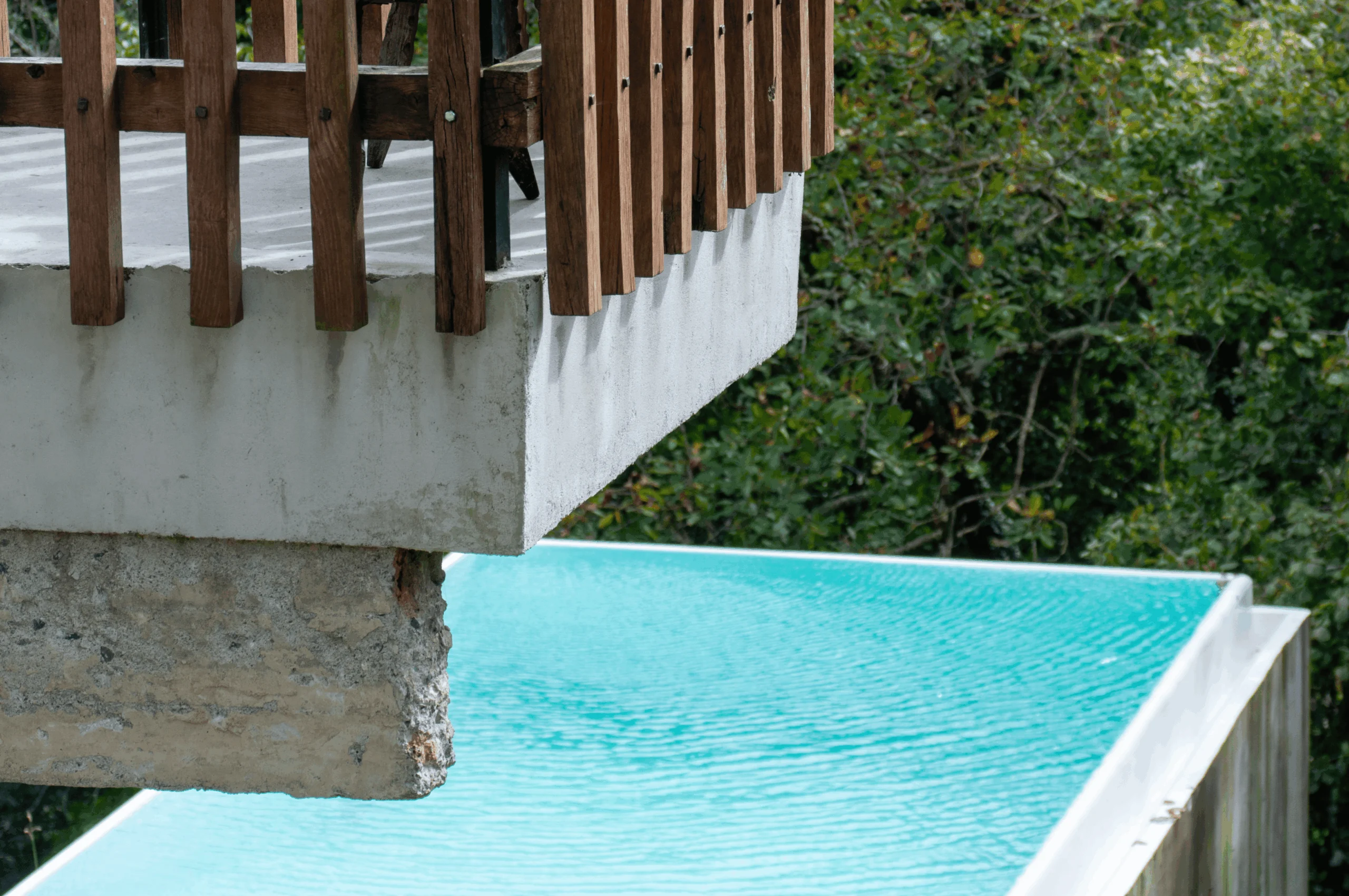 Balcón de hormigón con barandilla de madera sobre el borde de la piscina.