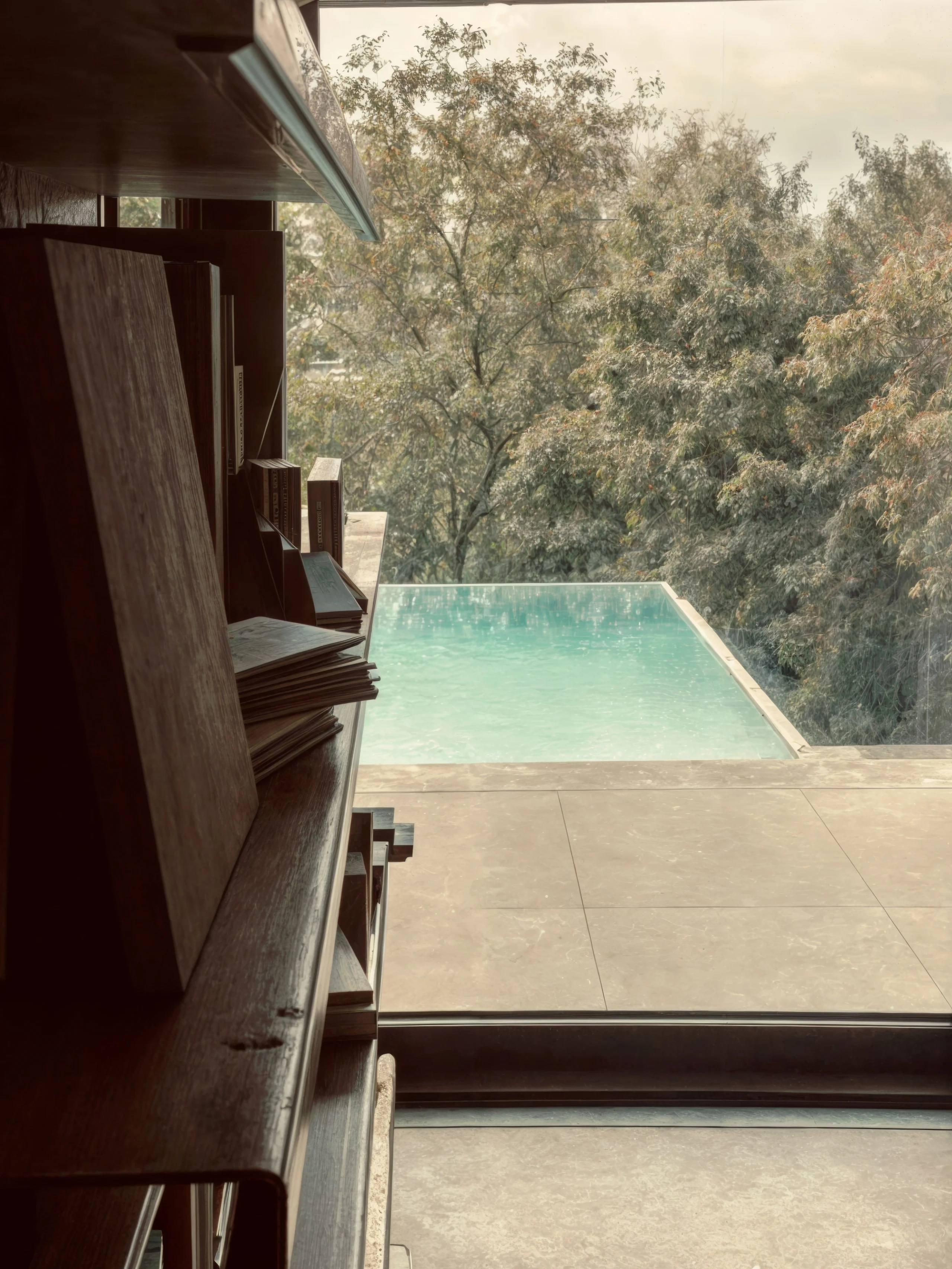 Piscina vista a través de un ventanal, junto a una estantería de madera.